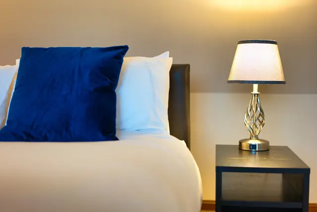 Close-up of navy velvet cushions on white pillows beside a crystal bedside lamp