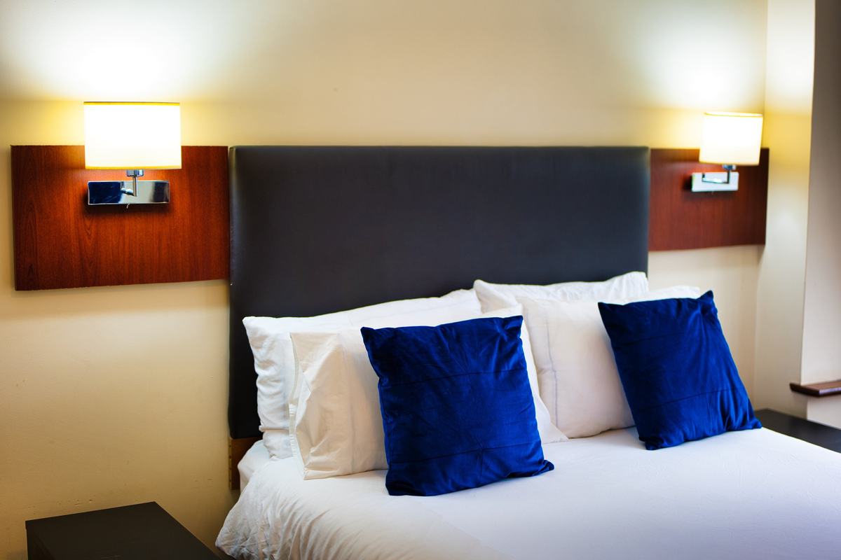 Double bed with white linen and navy velvet cushions between two warm wall lights and a padded headboard
