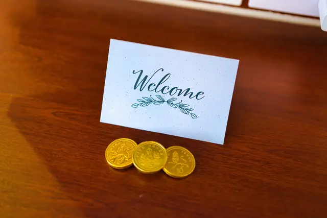 A handwritten-style welcome card with gold chocolate coins on a wooden desk